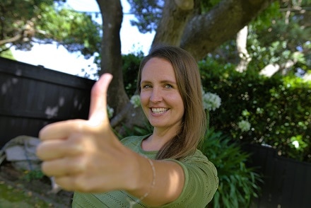 German teacher Jana standing in garden with thumbs up